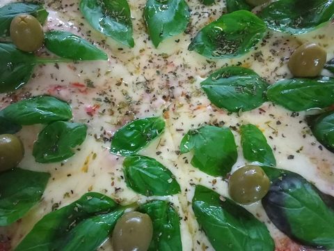 Pizza con hojas de albahaca y aceitunas